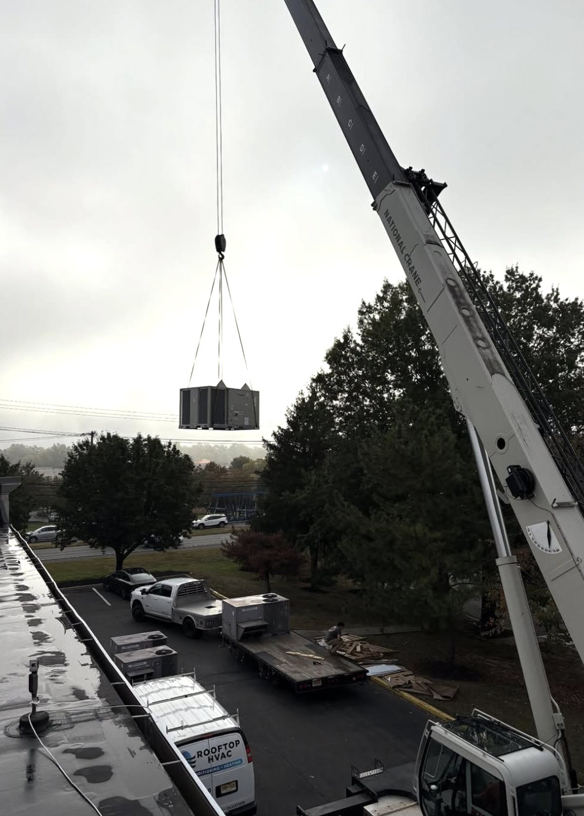 Rooftop unit carried by crane over the parking lot of a retail center