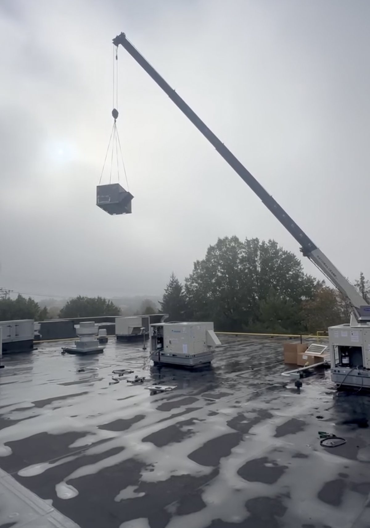Rooftop unit suspended from a crane above a commercial roof