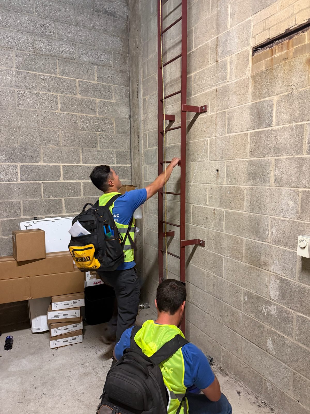 Rooftop HVAC technicians accessing a commercial roof by fixed ladder
