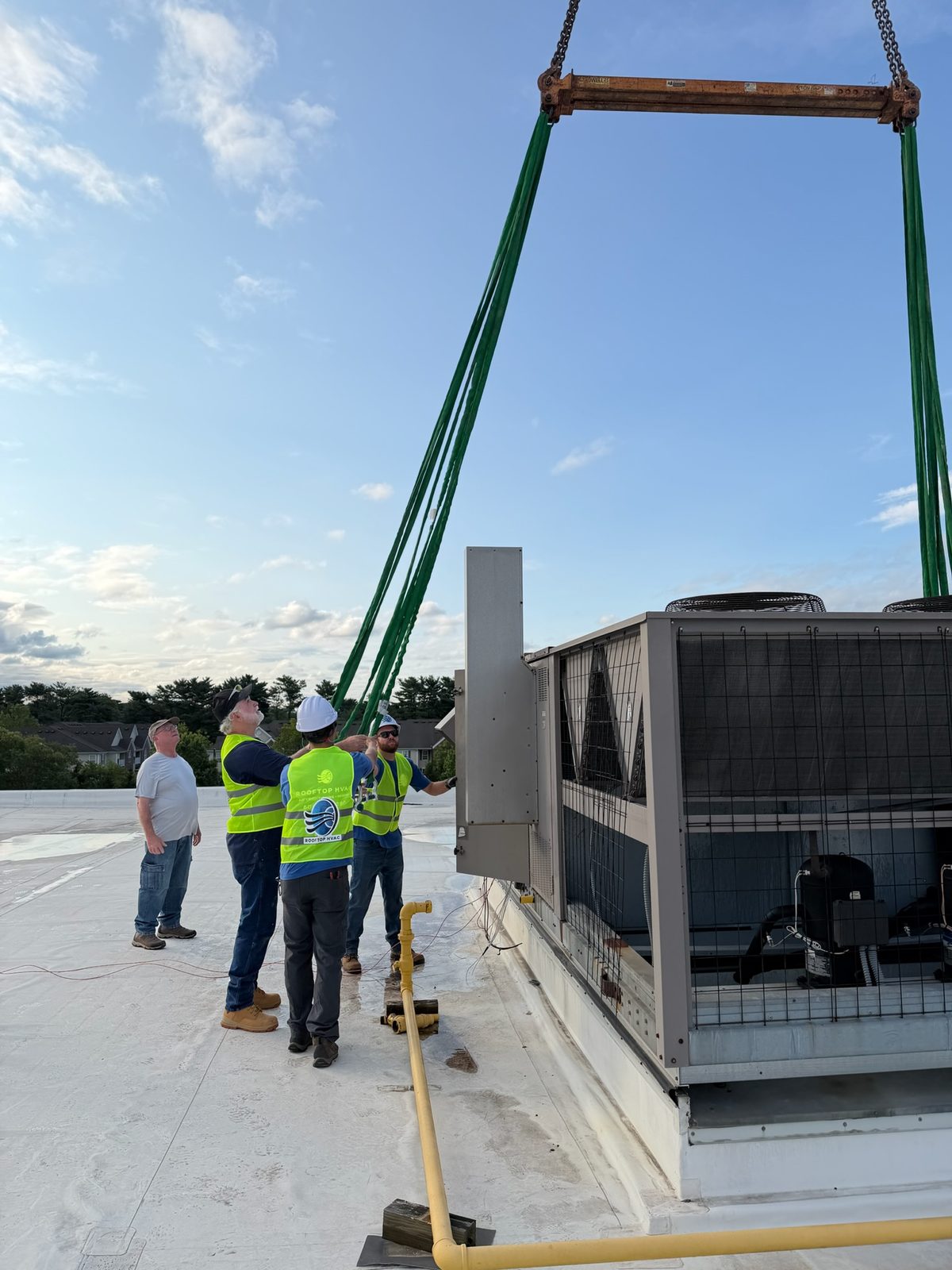 New rooftop unit being craned in alongside existing equipment on a commercial roof