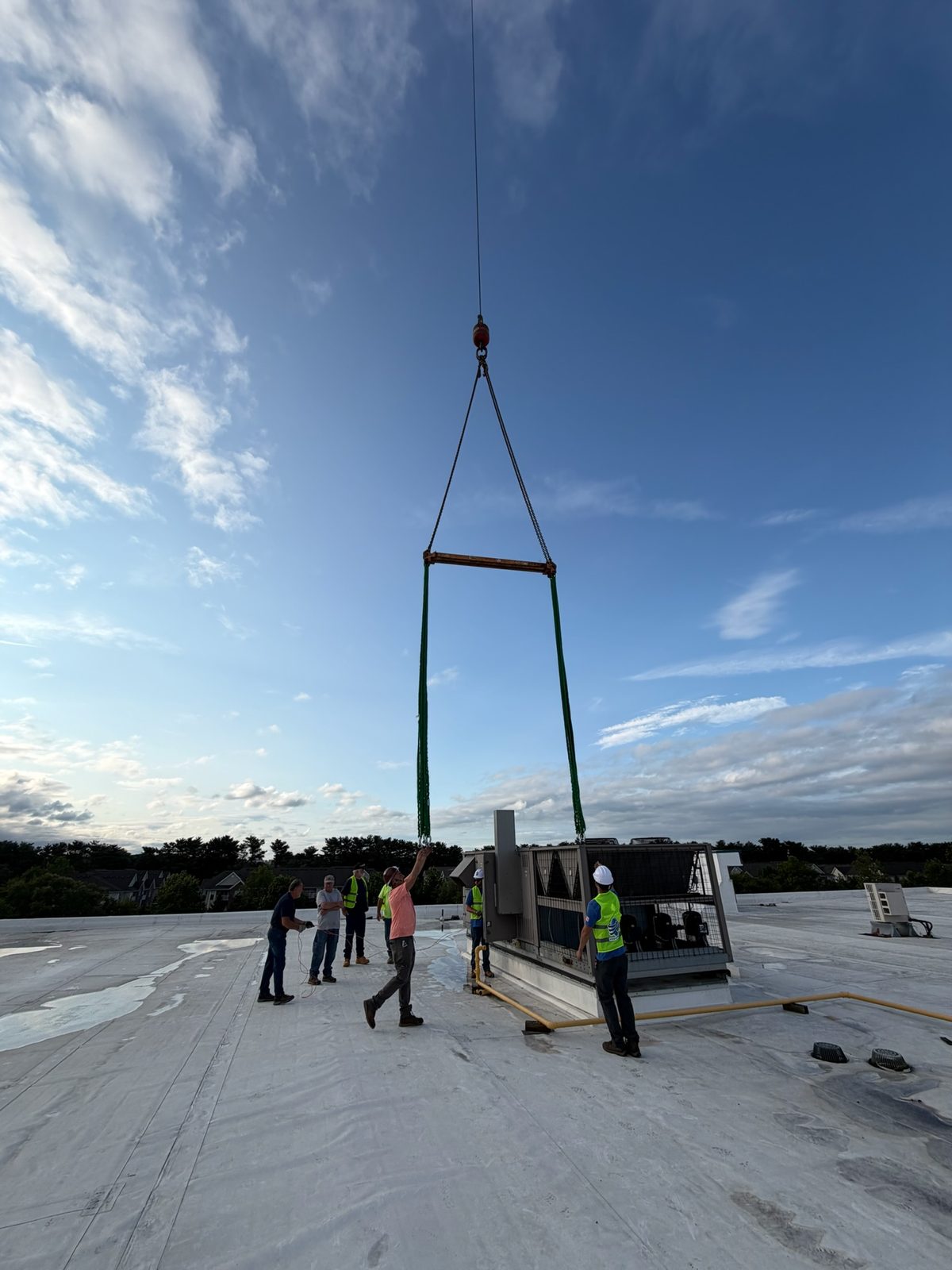 Crane rigging lowering a commercial rooftop unit onto a warehouse roof