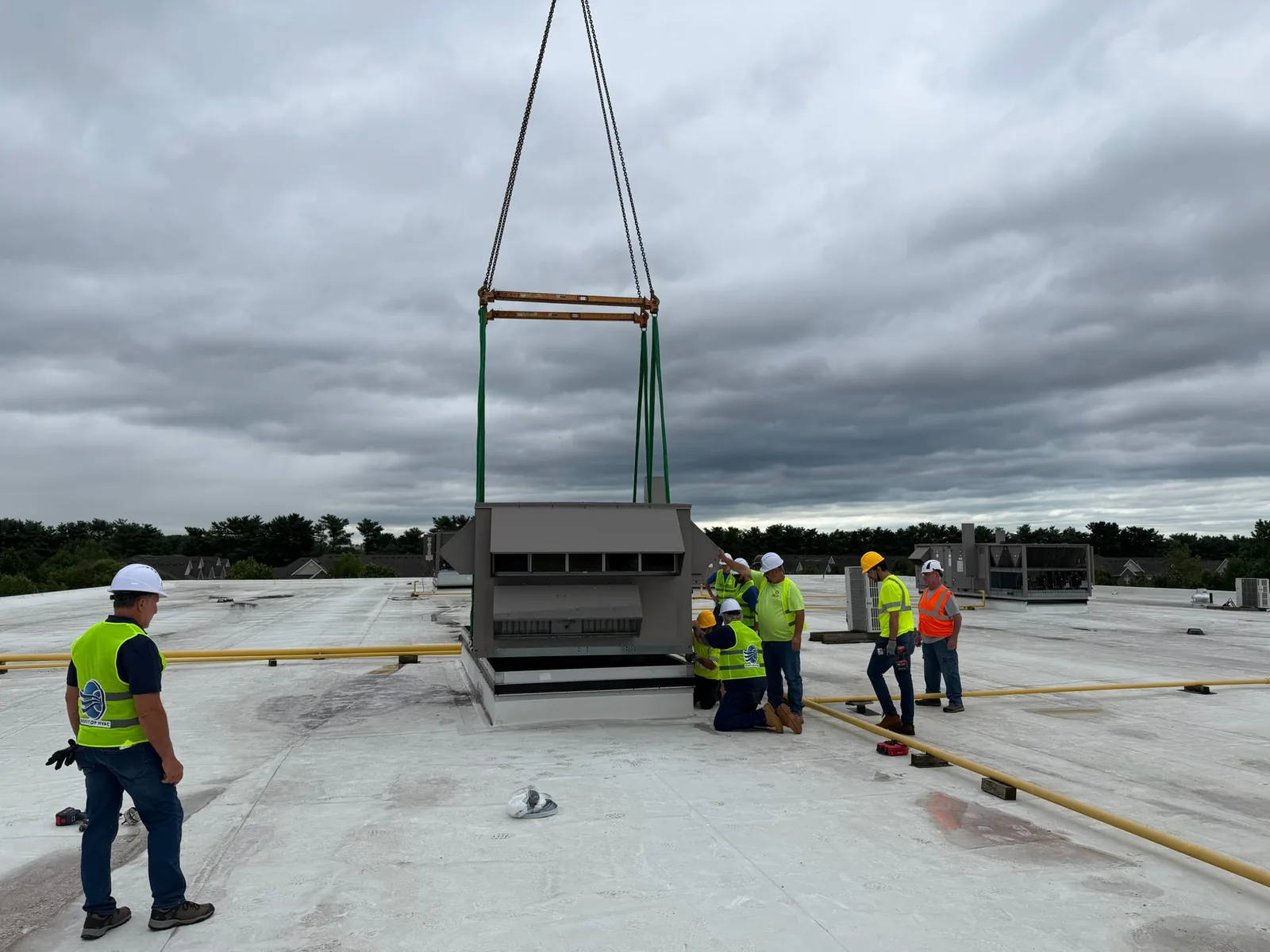 Rooftop HVAC crew guiding a rigged rooftop unit into position during a commercial RTU replacement