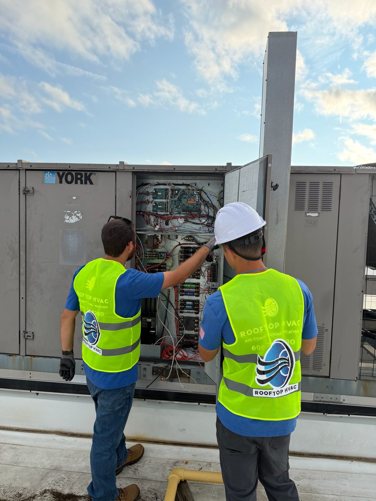 Rooftop HVAC technicians diagnosing the electrical panel of a York commercial rooftop unit